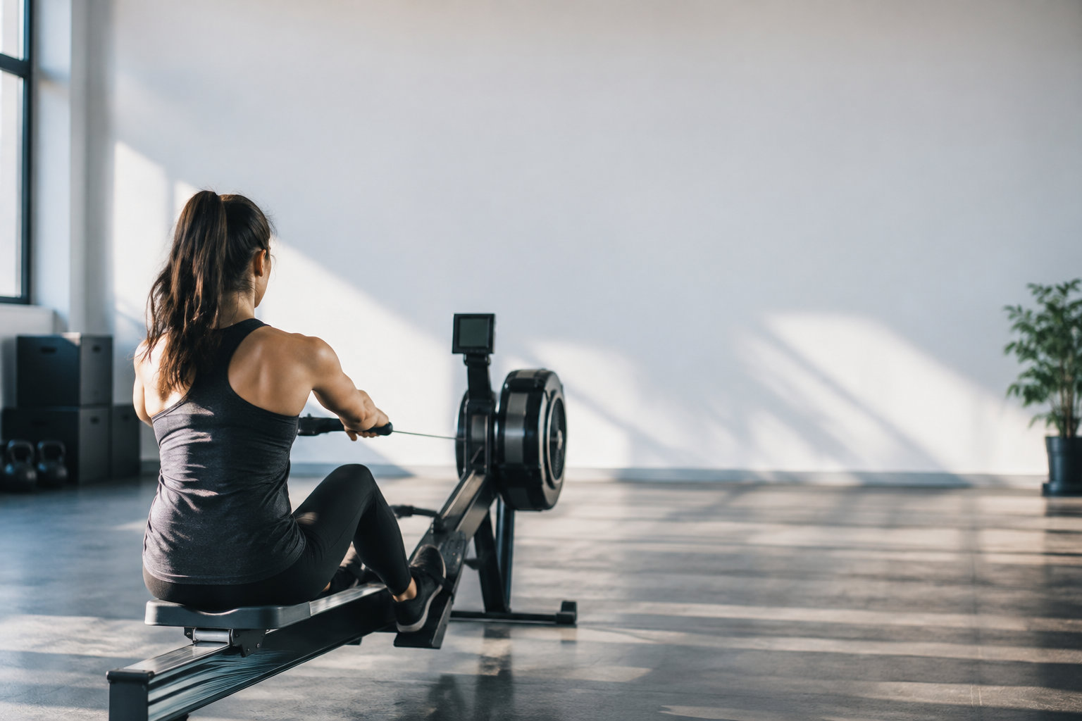Une femme de dos fait du rameur dans une salle de sport lumineuse et minimaliste.